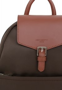 Sac à dos en tissu marron avec un rabat en cuir lisse marron, des accessoires en boucle argentée et un logo embossé "HEXAGONA PARIS" sur le devant.