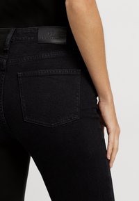 Svarta denimjeans med hög midja, en mjuk textur och en rektangulär bakficka. Midjebandet har en märkesskylt i läder.