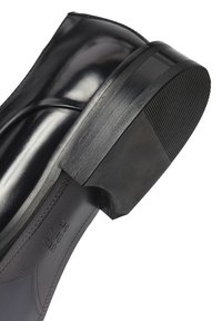 Zwarte gepolijste leren zool en hak van een nette schoen met zichtbare stiksels en een gestructureerde rubberen hakdop.