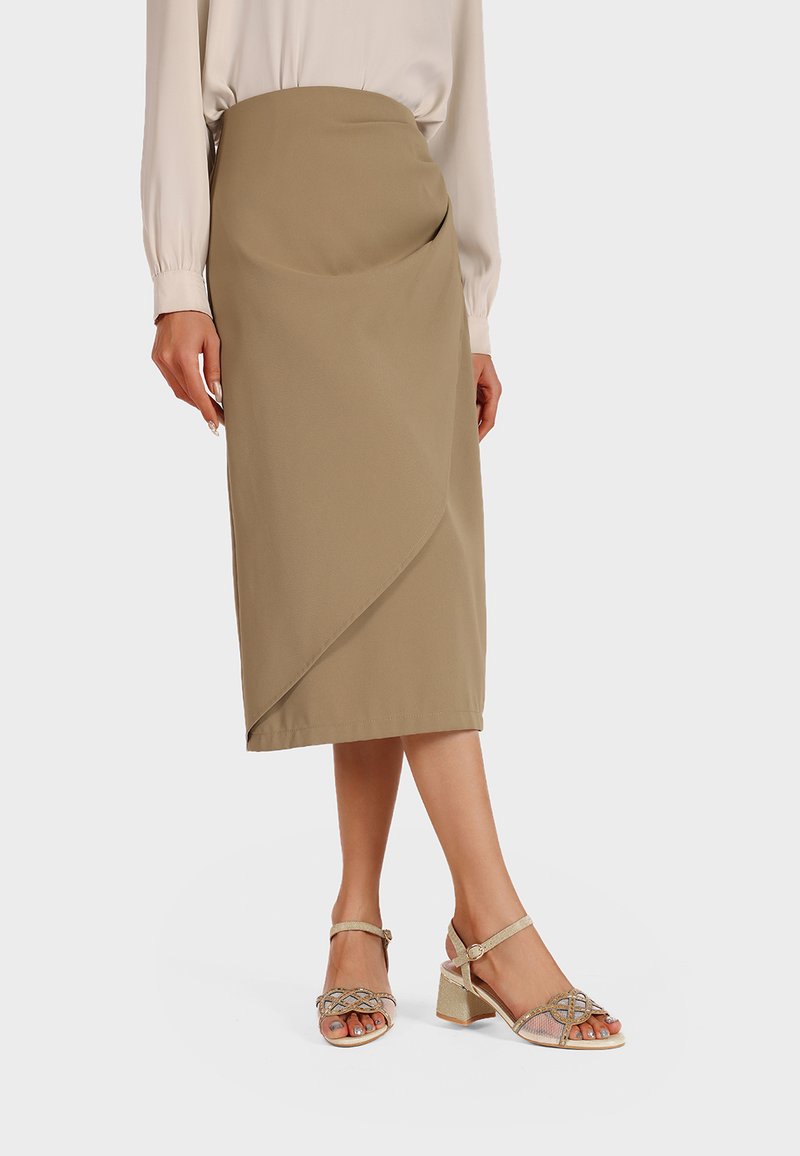 Gonna midi beige con un davanti drappeggiato, abbinata a sandali metallici con cinturini e tacco a blocco, dotati di dettagli decorativi. Texture liscia.