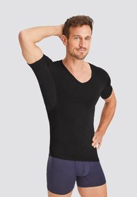 Black short-sleeve V-neck shirt, made of soft fabric. Features a fitted design and visible seams. Model poses with one arm raised.