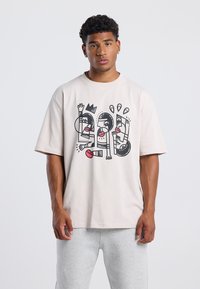 Light beige oversized t-shirt made of cotton, featuring a bold black and red graphic design with abstract human figures and elements.