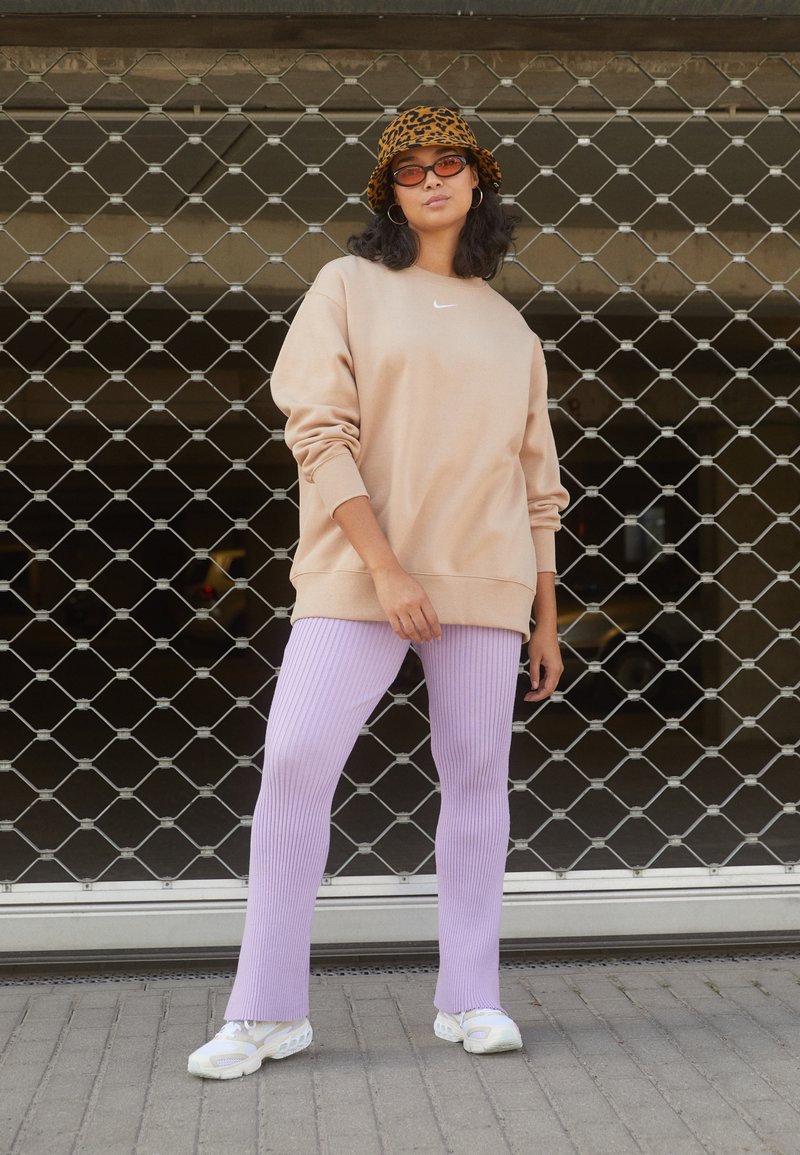 Sweat-shirt beige oversize avec un petit logo blanc, associé à un pantalon lavande côtelé et des baskets blanches. Chapeau seau à imprimé léopard noir et orange.