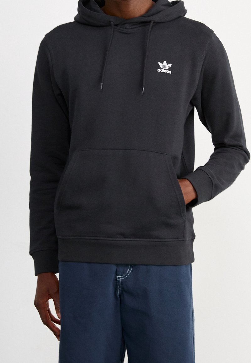 Sudadera gris oscuro hecha de un tejido suave, con un bolsillo frontal, capucha con cordón y un pequeño logo blanco en el pecho.