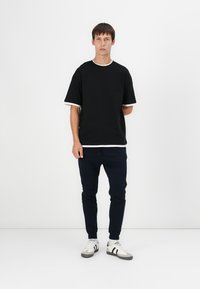 Schwarzes T-Shirt mit kurzen Ärmeln und kontrastierendem weißen Kragen, kombiniert mit marineblauen Jogginghosen und weißen Sneakers mit grauen Akzenten.