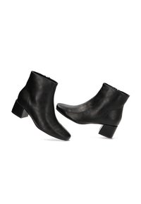 Botas de cuero negras hasta el tobillo con tacones cuadrados y cremalleras laterales, colocadas sobre un fondo blanco.