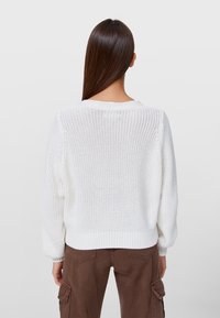Bílý pletený svetr s volným střihem, žebrovanými manžetami a spodním lemem. Obsahuje texturovaný design s otevřeným pletením a širokým výstřihem.