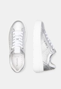 Baskets métalliques argentées avec une finition lisse, des lacets blancs, des détails perforés et une épaisse semelle blanche. Deux chaussures montrées de dessus.