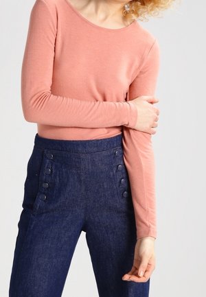Langærmet, koralrød top kombineret med højtaljede, mørk indigoblå denimbukser med knapdetaljer langs siderne. Glat, tætsiddende silhuet.