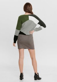 Pull en tricot avec des blocs de couleurs vert, gris, blanc et noir. Associé à une jupe en daim gris et des bottines à talons noires.