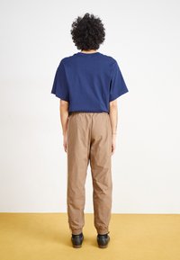 T-shirt de algodão azul-marinho, com corte descontraído, mangas curtas. Calças castanhas com cintura elástica e tornozelos com punhos. Sapatos pretos com solas de borracha.