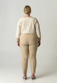 Beige, taillierte Hose mit hoher Taille, kombiniert mit einer cremefarbenen Bluse mit dreiviertellangen Ärmeln und quadratischem Ausschnitt. Glatte Textur.