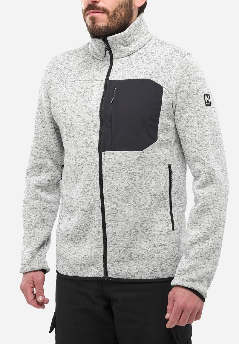 Veste en polaire grise clair avec une poche poitrine zippée noire, des poches latérales, un col montant et des accents zippés noirs. Tissu texturé.