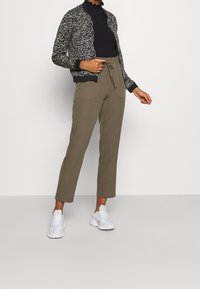 Bílý a černý bomber s vlnkovaným vzorem, žebrované manžety, černý vysoký límec, olivově zelené tepláky s bočními kapsami, bílé tenisky.