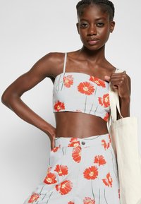 Top cropped floral cinza com padrão de flores vermelhas, apresentando alças finas. Combinado com calças de cintura alta exibindo o mesmo design floral.