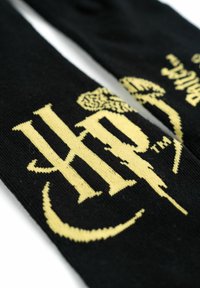 Calze nere di maglia con un prominente logo "HP" giallo e un design a forma di fulmine. Texture liscia con cuciture dettagliate.
