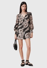 Svart klänning med beige paisleymönster, lång puffärmar, V-ringning och rynkad midja. Matchad med en svart handväska och platta sandaler.