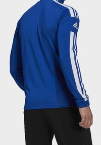 Haut de sport bleu à manches longues avec des accents blancs à trois bandes sur les manches, doté d'un col haut et de poignets élastiques pour un ajustement près du corps.