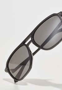 Ochelari de soare cu un cadru din plastic negru, lentile rectangulară cu polarizare închisă și detalii discrete pe brațe.