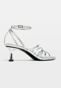 Sandale argentée à lanières fines, avec boucle à la cheville et un talon bloc noir et blanc. Design à bout ouvert avec une finition élégante.