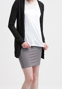 Cardigan lungo nero, camicia bianca a rete e gonna grigia aderente. L'outfit presenta materiali morbidi e una consistenza liscia.