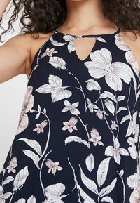 Blommig klänning med marin bakgrund, prydd med vita och rosa blommönster, halterneck och en nyckelhålsknyppling vid bröstet.