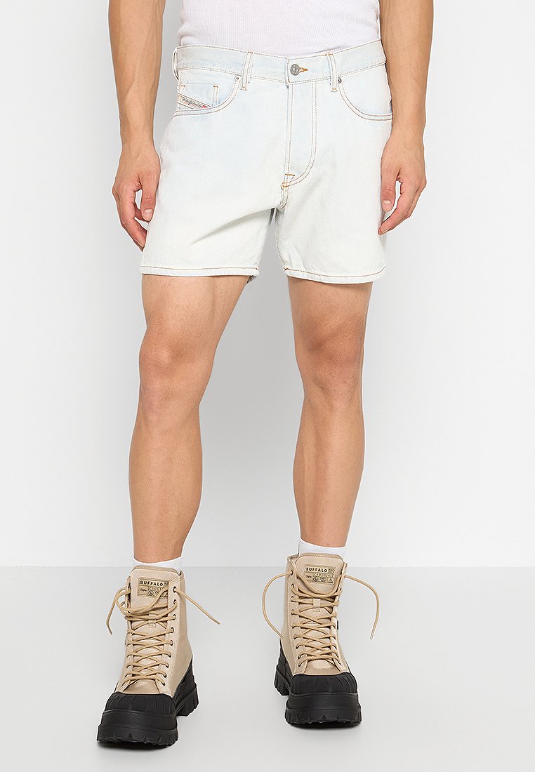 Lichtblauwe denimshorts met een klassiek vijf-pocket ontwerp, afgewerkt met oranje stiksels. Gekleed met tan-kleurige veterschoenen.