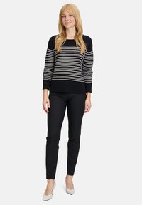 Gestreifter Pullover in Schwarz-Weiß mit strukturiertem Strick, gerippten Bündchen und Saum, kombiniert mit enganliegenden schwarzen Hosen und hellen Absätzen.