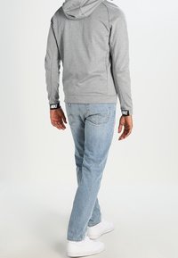 Grå huvtröja med svarta Nike-detaljer, kombinerad med ljusblå jeans och vita sneakers, sedd bakifrån.