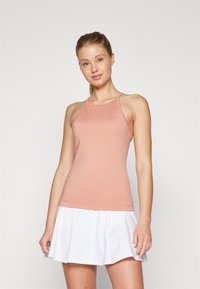 Top sportivo atletico rosa chiaro con spalline sottili e design senza cuciture, abbinato a una gonna bianca plissettata con piccole perforazioni.