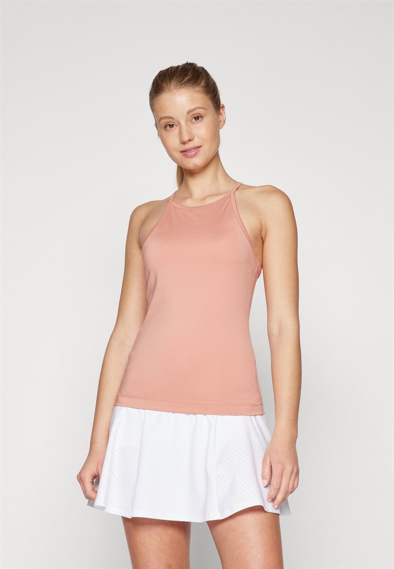 Top sportivo atletico rosa chiaro con spalline sottili e design senza cuciture, abbinato a una gonna bianca plissettata con piccole perforazioni.