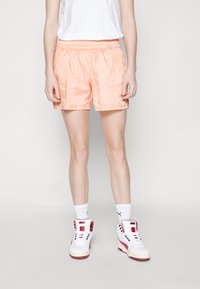 Šortky v broskvové barvě, lehké atletické, s elastickým pasem a bočními kapsami, spárované s bílými a červenými vysokými teniskami.