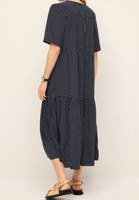 Laivansinis pilkos taškeliais suknelė su trumpomis rankovėmis, sluoksniuota konstrukcija ir laisvu siluetu. Yra apvalus iškirpimas ir tekstūruotas audinys.