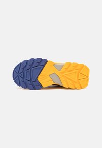 Trail running shoe outsole in blue, yellow, and gray. Features textured grip with a zigzag pattern and angular design for traction.