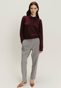 Burgundský svetr s polo límcem a detailem knoflíků v kombinaci se šedými kalhotami. Hnědé boty s špičatou špičkou dotvářejí outfit.