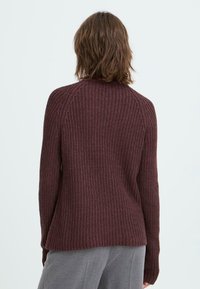 Maglione a maglia bordeaux con un motivo testurizzato, maniche raglan e scollatura rotonda. L'orlo è leggermente curvato nella parte inferiore.