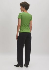 Groene T-shirt met korte mouwen en een ronde halslijn, gecombineerd met hoge zwarte broeken. Soepele textuur, aansluitend op de schouders.