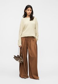 Pull beige côtelé, pantalon marron à jambes larges, et sac à main imprimé léopard. Détails remarquables : plis sur le pantalon et sac à motifs.