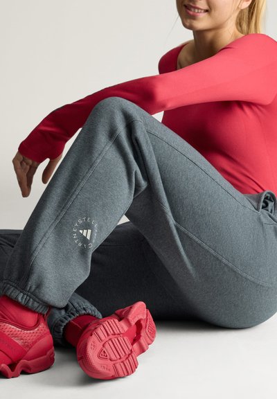 Γυναίκα κάθεται στο πάτωμα φορώντας γκρι adidas Stella McCartney φόρμα, κόκκινη μακρυμάνικη μπλούζα, κόκκινες κάλτσες και κόκκινα αθλητικά παπούτσια.