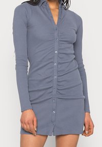 Långärmad, grå ribbad klänning med krage, knappstängning och rynkade detaljer längs framsidan för extra textur.