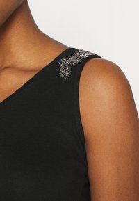 Svart ärmlös topp med en texturerad pärldetalj på vänster axel, tillverkad av mjukt bomullsmaterial och med en figurnära design.