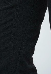 Tela de mezclilla negra con un patrón de espiga, que cuenta con costuras curvas y una textura suave. El detalle en primer plano enfatiza la estructura de la tela.