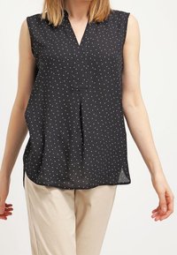 Top nero senza maniche con scollatura a V, caratterizzato da un sottile motivo a pois bianchi e una vestibilità rilassata, realizzato in tessuto leggero.