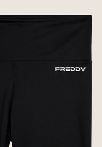 Leggings neri realizzati in tessuto elasticizzato con una fascia in vita ampia. Il nome del marchio "FREDDY" è stampato in bianco sul lato sinistro.