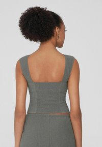 Crop top gris avec un dos carré, à coupe ajustée et en tissu texturé. Doté de larges bretelles et d'un dos froncé pour un confort supplémentaire.