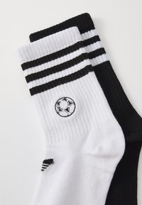 Mustad ja valged sokid, millel on triibuline muster. Valgel sokil on ümmargune broderitud jalgpallilogo ja sooniktekstuur.