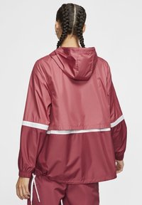 Veste coupe-vent bordeaux avec capuche, poignets élastiques et bandes réfléchissantes blanches sur le haut du dos et les manches. Ourlet à cordon de serrage ajustable.