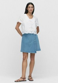 Vitt ögonlets cropped linne med korta ärmar och knytframsdetalj, parat med en ljusblå jeans A-linjeformad kjol med rå fåll.