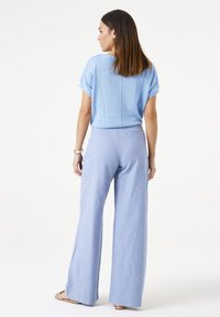 Hellblaues Stricktop mit kurzen Ärmeln, kombiniert mit hellblauen weit geschnittenen Hosen. Das Outfit zeichnet sich durch eine lockere Passform und einen strukturierten Stoff aus.