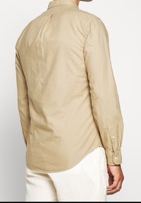 Jasno beżowa, długo-sleeve koszula z wyraźnym kołnierzykiem, zapięciem na guziki przy mankietach i zaokrąglonym dołem. Wykonana z gładkiego materiału o jednolitej fakturze.